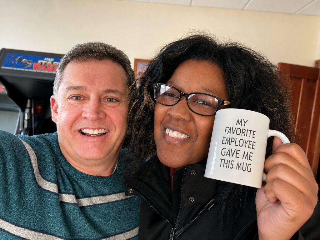 Two Lanex team members smiling together in the office while holding a humorous coffee mug, reflecting the company's friendly workplace culture.